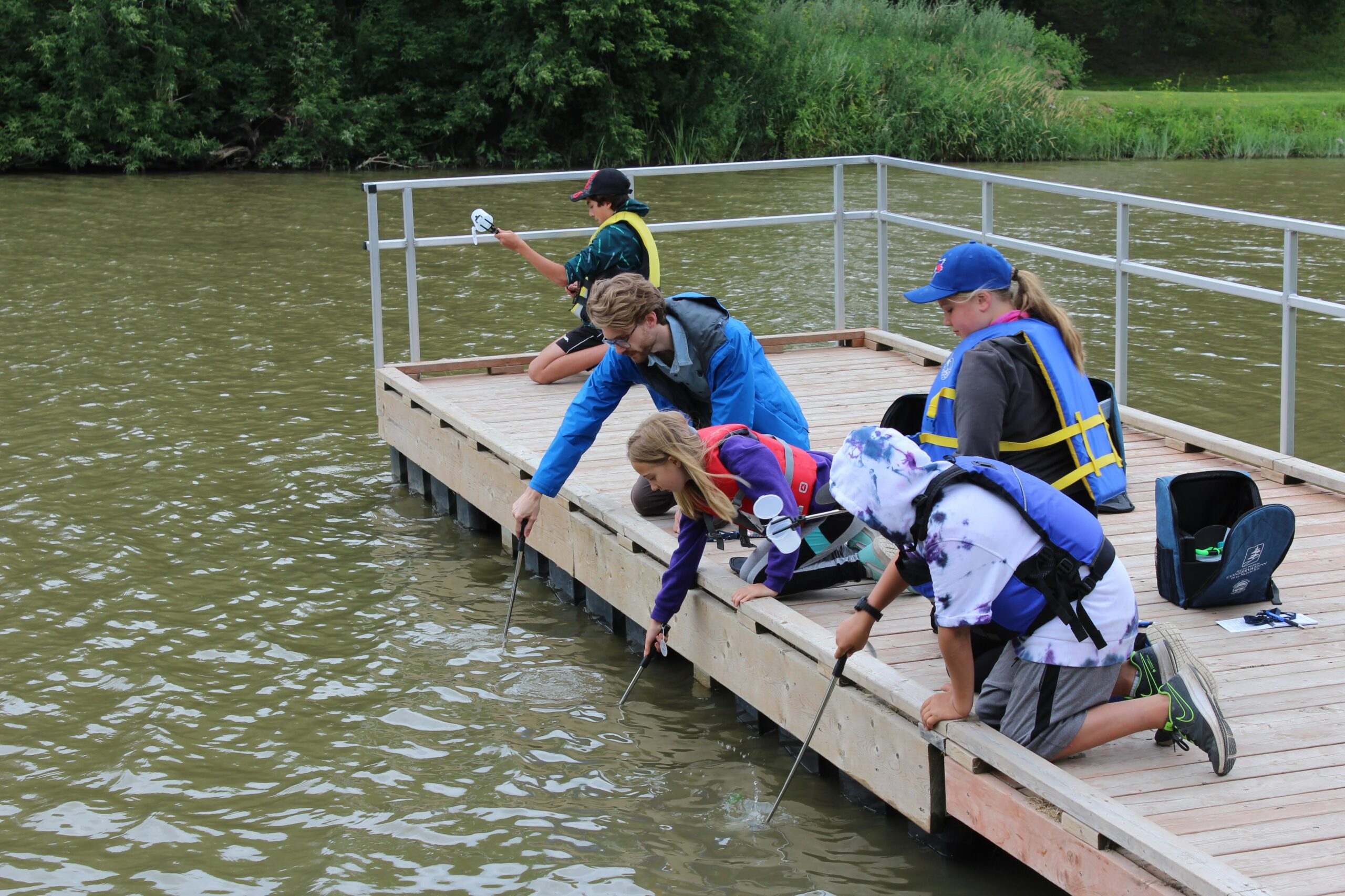 A group of water testers reaching into the water from a dock to collect samples.